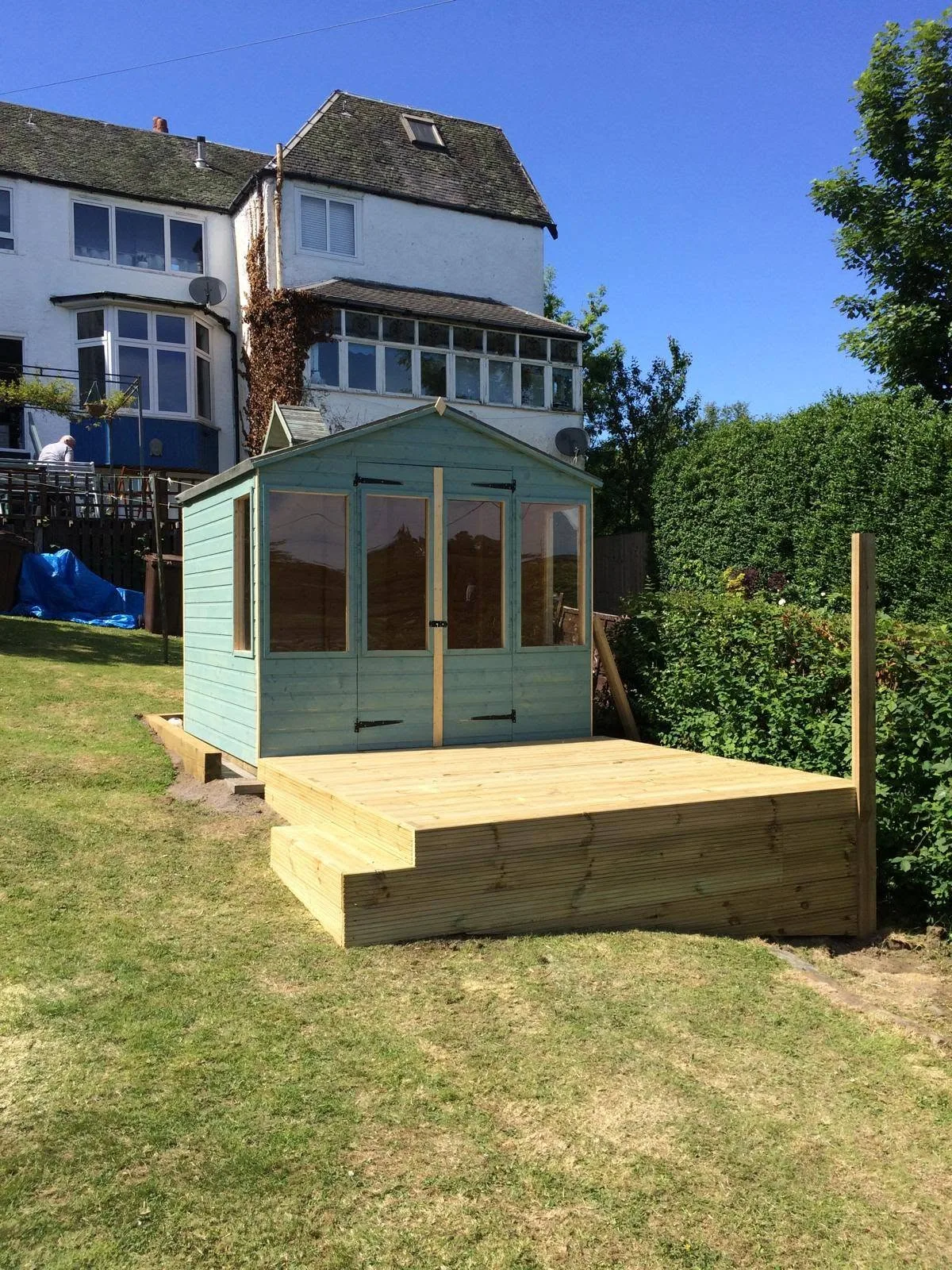 Painted summerhouse with raised timber decking in a sloping garden